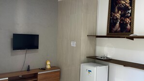 Una sala de estar con televisor de pantalla plana, un sofá, un refrigerador pequeño y un cuadro en la pared.