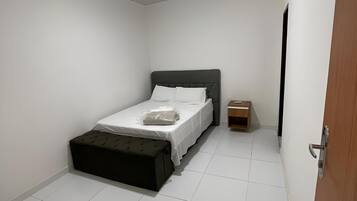 A small, neatly arranged bedroom with a single bed, a bedside table, a small cabinet, and a door.