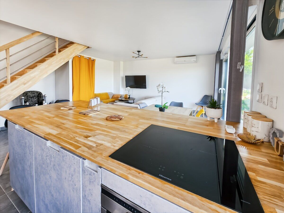 Une cuisine moderne dotée d’un îlot central, d’appareils électroménagers intégrés et d’un escalier menant à un niveau supérieur.