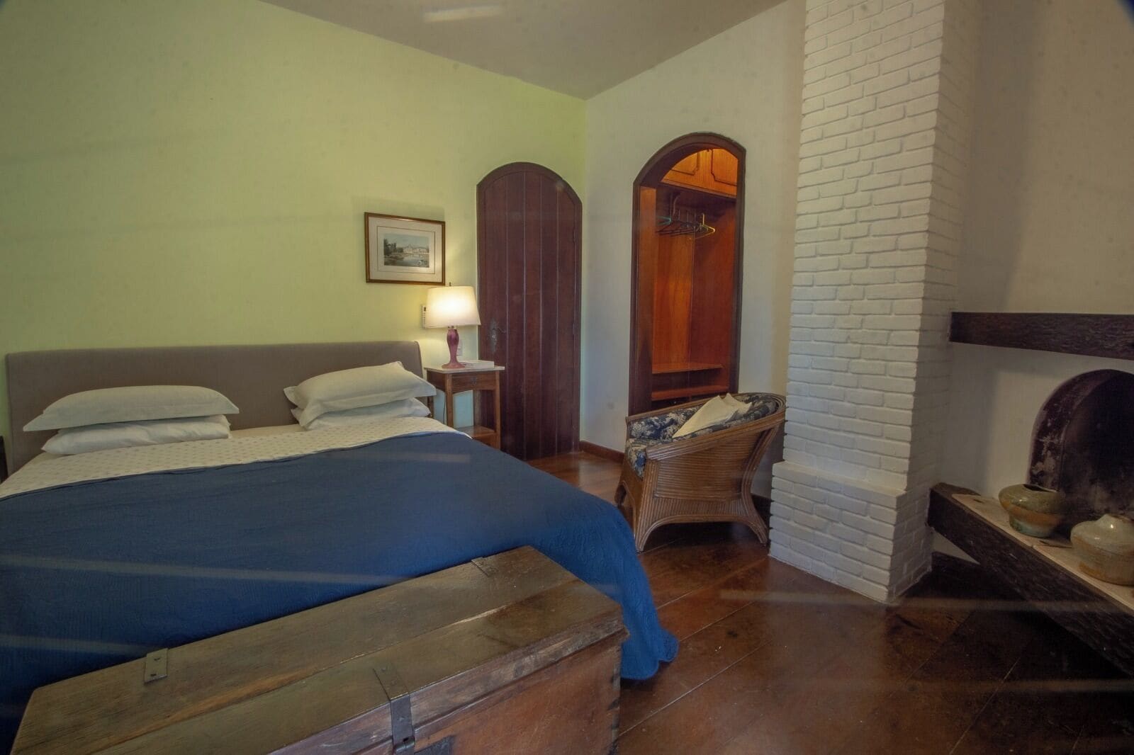 Um quarto com cama, poltrona, luminária e lareira.
