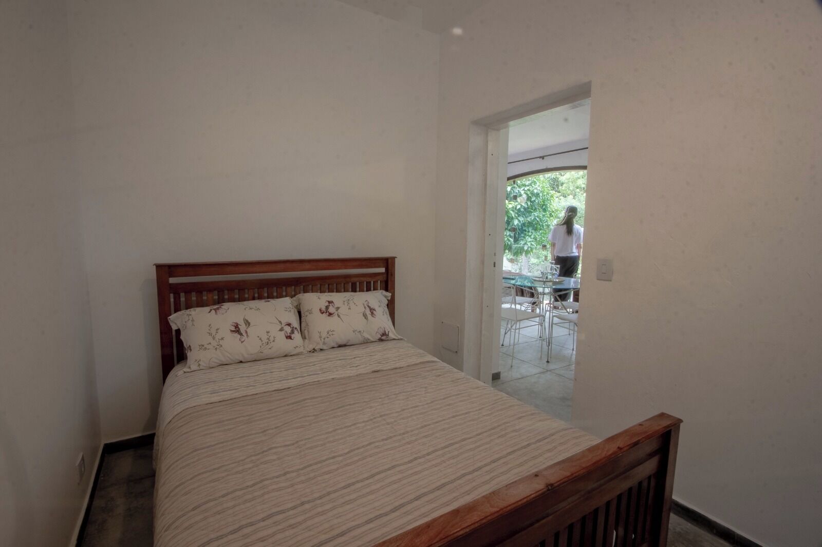Quarto com cama de madeira, mesa de cabeceira e vista para um pátio externo.