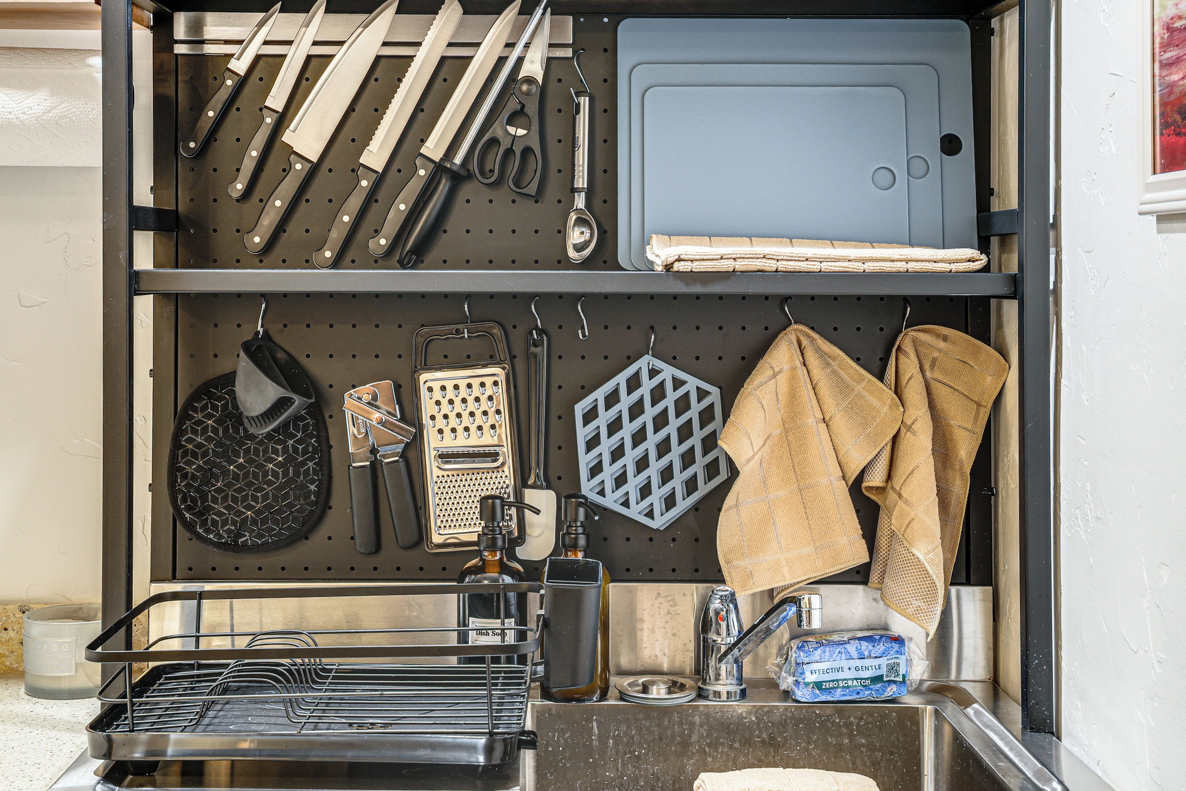 A kitchen with utensils, a cutting board, a grater, a bottle, and a dish soap dispenser.