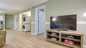 Un salon équipé d’un téléviseur à écran plat, d’un canapé, d’un meuble de rangement en bois contenant des livres et d’un coin buanderie avec un lave-linge et un sèche-linge.