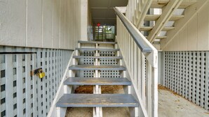 Un escalier avec une rampe métallique, menant à une porte de sortie surmontée d’un feu rouge d’urgence.