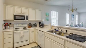 Une cuisine avec des meubles blancs, un four à micro-ondes, une cuisinière, un lave-vaisselle et un évier surmonté d’un tapis noir.