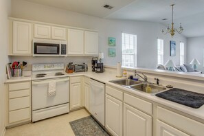 A kitchen with white cabinets, a microwave, stove, dishwasher, and a sink with a black mat. - Golf Resort Stay in Sunset Beach: Pool, Balcony (Sunset Beach)