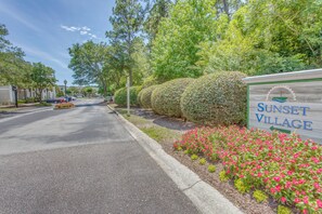 A street sign for Sunset Village with a road lined with trees and flowers. - Golf Resort Stay in Sunset Beach: Pool, Balcony (Sunset Beach)