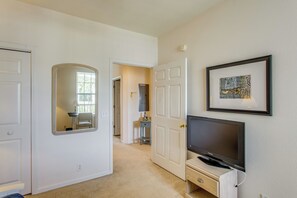 Ein Zimmer mit Fernseher auf einem Schrank, einem gerahmten Bild an der Wand und einer Tür zu einem anderen Raum.