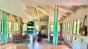 Ein geräumiges Zimmer mit Holzboden, einer Essecke, Trainingsgeräten und großen Fenstern.
