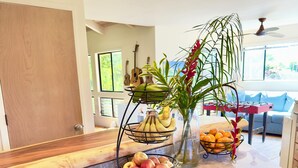 Eine Küchenarbeitsplatte mit einer Obstschale mit Bananen, Äpfeln und Orangen, einer Vase mit Blumen und einer Gitarre im Hintergrund.
