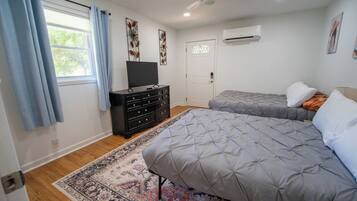 Un dormitorio con dos camas, un aparador, un ventilador de techo y un equipo de aire acondicionado.