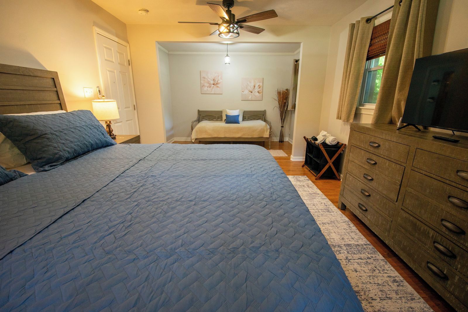 Une chambre à coucher comprenant un lit, une commode, un ventilateur de plafond et un téléviseur.