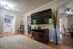 A living room with a flat-screen TV, a wooden entertainment center, a dining area with a table and chairs, and a hallway leading to another room. - Aiken Equestrian Dog Friendly  Bruce's Field (Aiken)