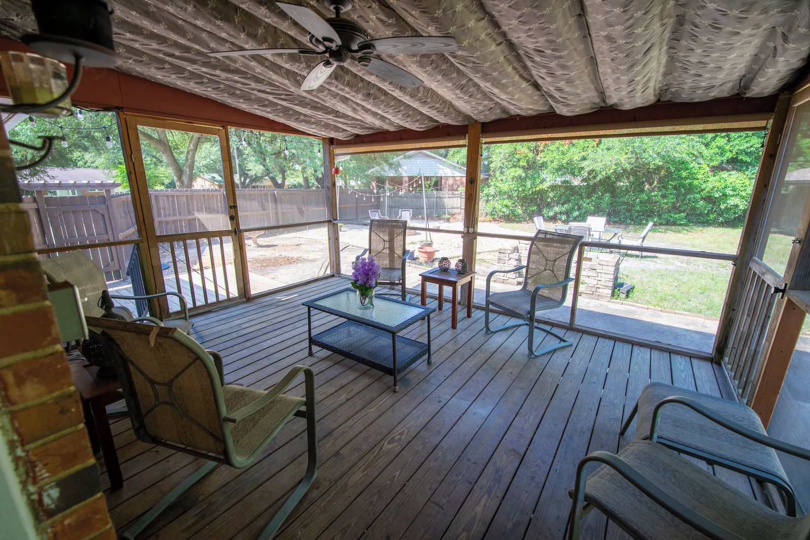 An outdoor patio with wooden flooring, metal chairs, a table, and a ceiling fan.