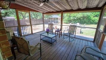 An outdoor patio with wooden flooring, metal chairs, a table, and a ceiling fan.