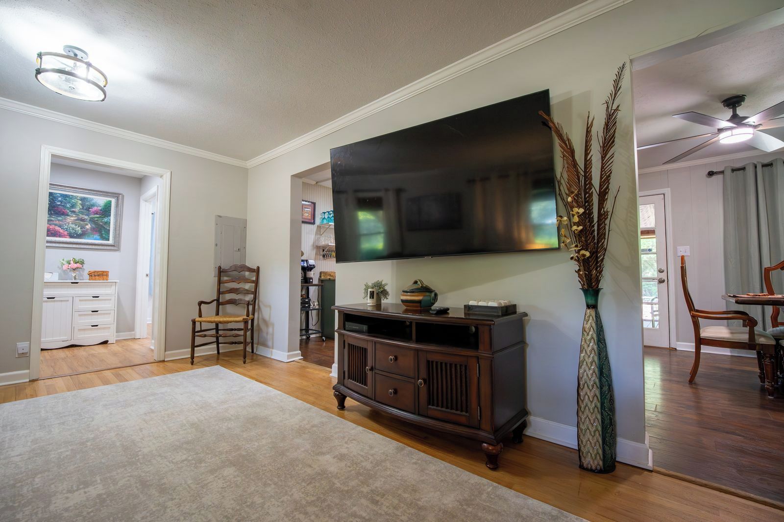A living room with a flat-screen TV, wooden furniture, a large vase, and a dining area with chairs.