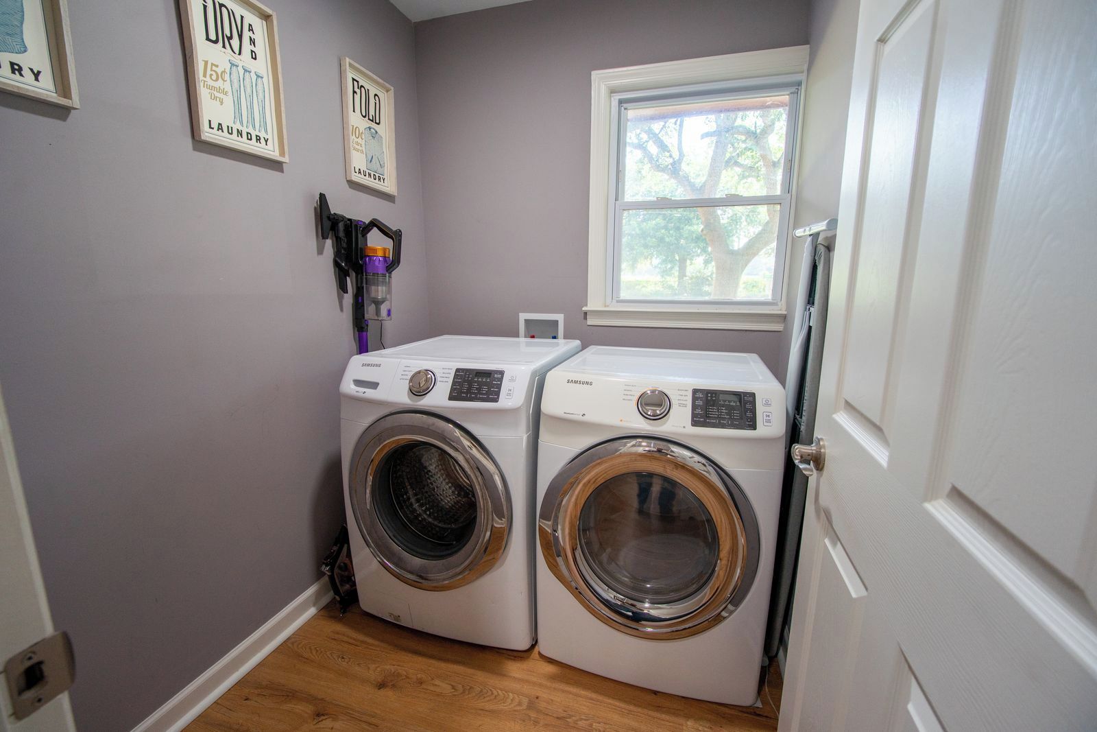 A laundry room with two white washing machines, a window, and a door.