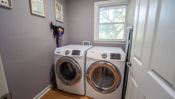 A laundry room with two white washing machines, a window, and a door.