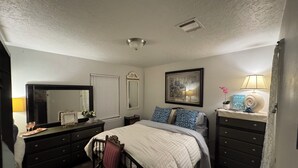 Um quarto com cama, cômoda, cadeira e espelho.