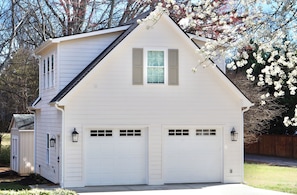 A two-story house with a garage, a small window on the second floor, and a light fixture on the garage door. - Prime Location Detached Garage Apartment (Greer)