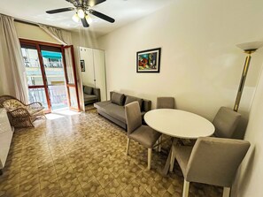 A living room with a sofa, a dining table with chairs, a ceiling fan, and a window with curtains. - Apartment Rubens by Interhome (Rapallo)