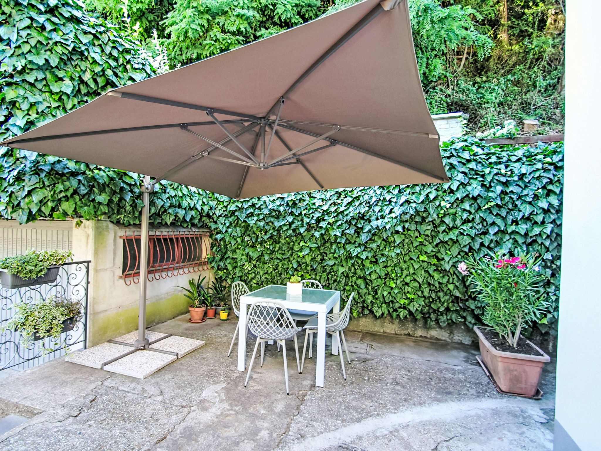 A patio with a table and chairs, a large umbrella, and a wall of greenery.