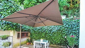 Un patio con mesa y sillas, un paraguas grande y una pared cubierta de vegetación.