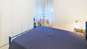 Un dormitorio con cama, escritorio, silla, ventana con cortinas y lámpara colgante.