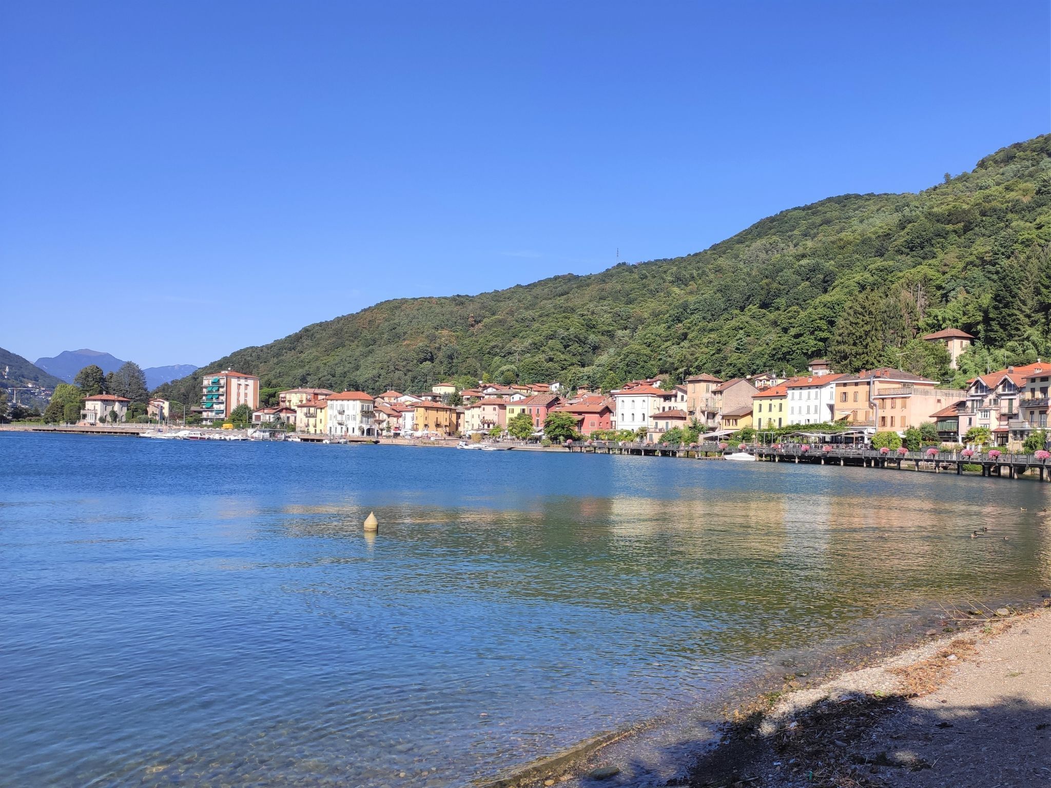 Une ville au bord d’un lac, avec des bâtiments qui bordent la rive, une jetée qui s’avance dans l’eau et des collines en arrière-plan.
