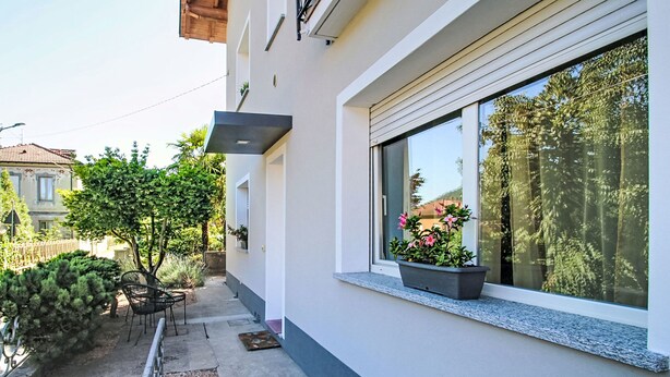 Un edificio moderno con balcón, un pequeño jardín y una ventana con planta.