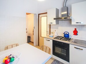 Una cocina con estufa a gas, horno, armarios blancos y un comedor con mesa y sillas.
