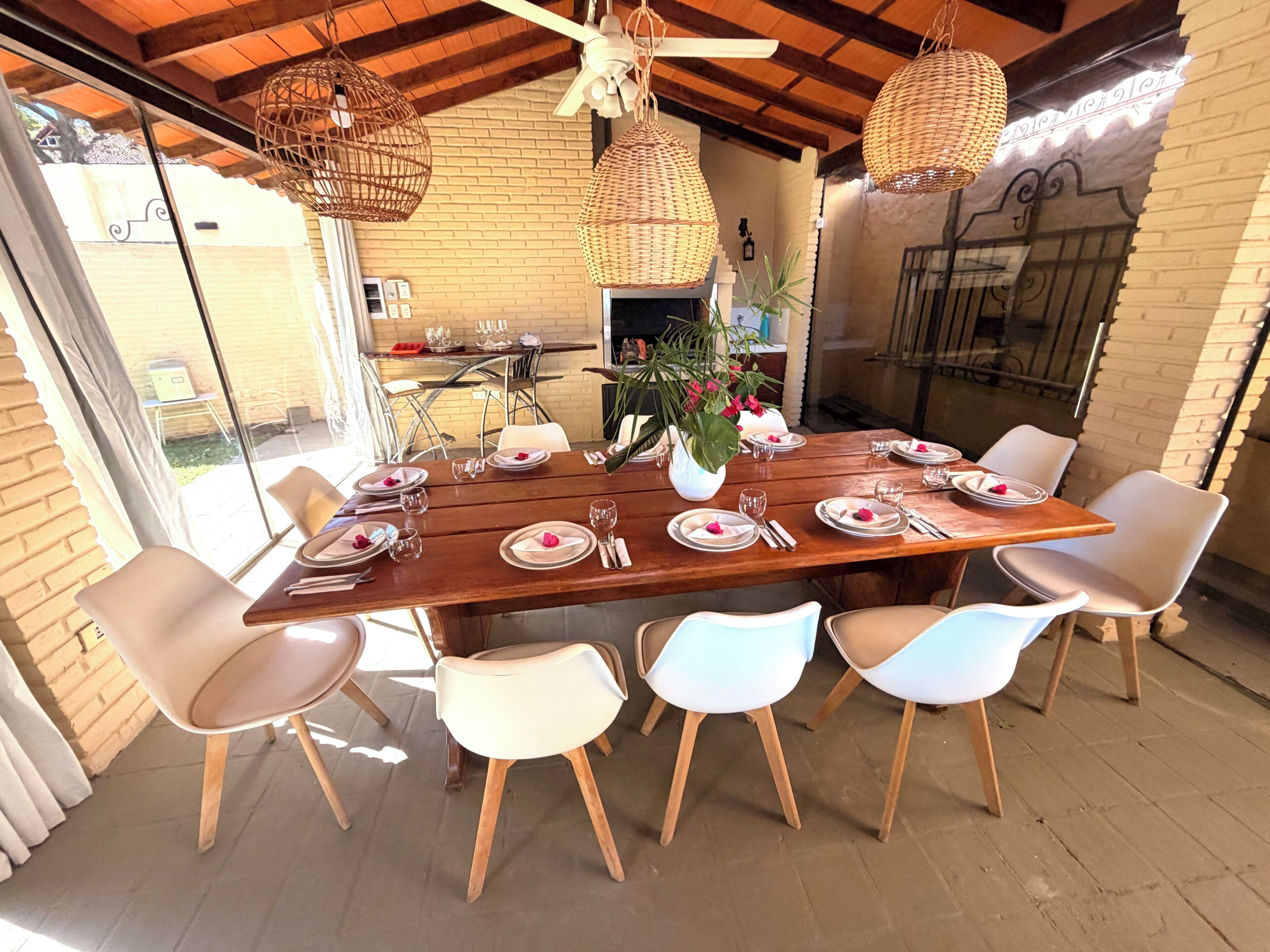 Comedor con una mesa de madera dispuesta para seis personas, rodeado de sillas blancas con patas de madera.