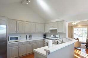 A modern kitchen with white cabinetry, a built-in microwave, a coffee maker, and a large island with a sink. - Excellent Location 3-Bedroom House on Large Quiet Lot (Greer)