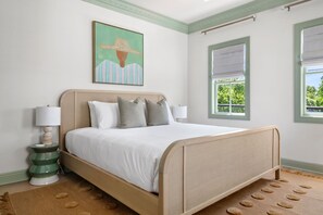 A bedroom with a bed, two bedside lamps, a painting, and two windows with blinds. - Designer Retreat | Pool + 4 King Suites (Charleston)