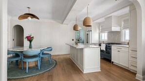 Une cuisine moderne avec des meubles blancs, un îlot central et un coin repas agrémenté de chaises bleues et d’une table ronde.