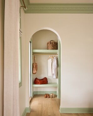 A hallway with a green archway leading to a closet with shelves, a hanging bag, and shoes. - Designer Retreat | Pool + 4 King Suites (Charleston)