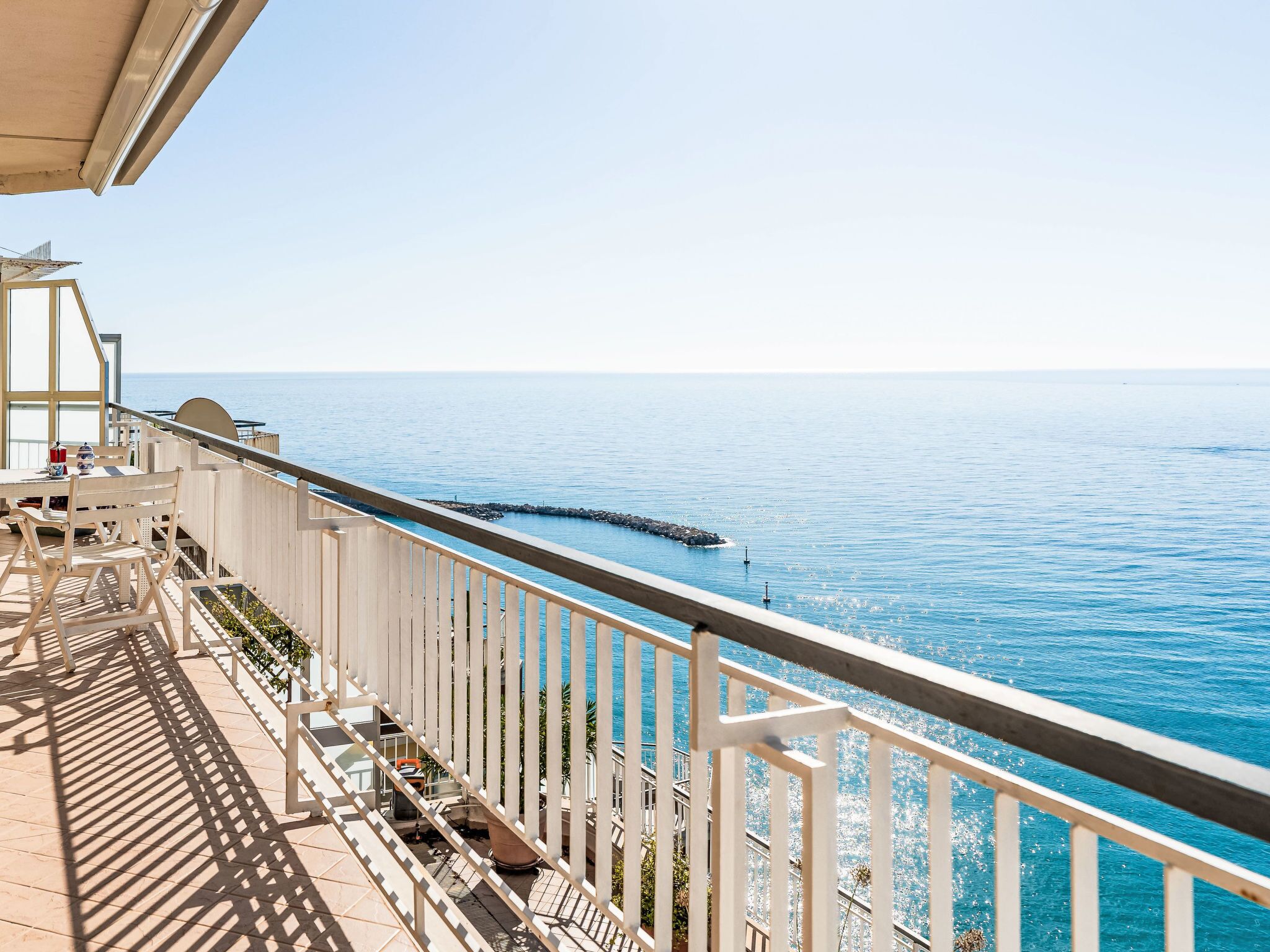 Ein Balkon am Meer mit Blick auf den Ozean, einem Geländer und einem Tisch mit Stühlen.
