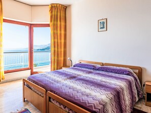 Ein Schlafzimmer mit Bett, Nachttisch, Lampe, einem Bild an der Wand und Meerblick vom Balkon.