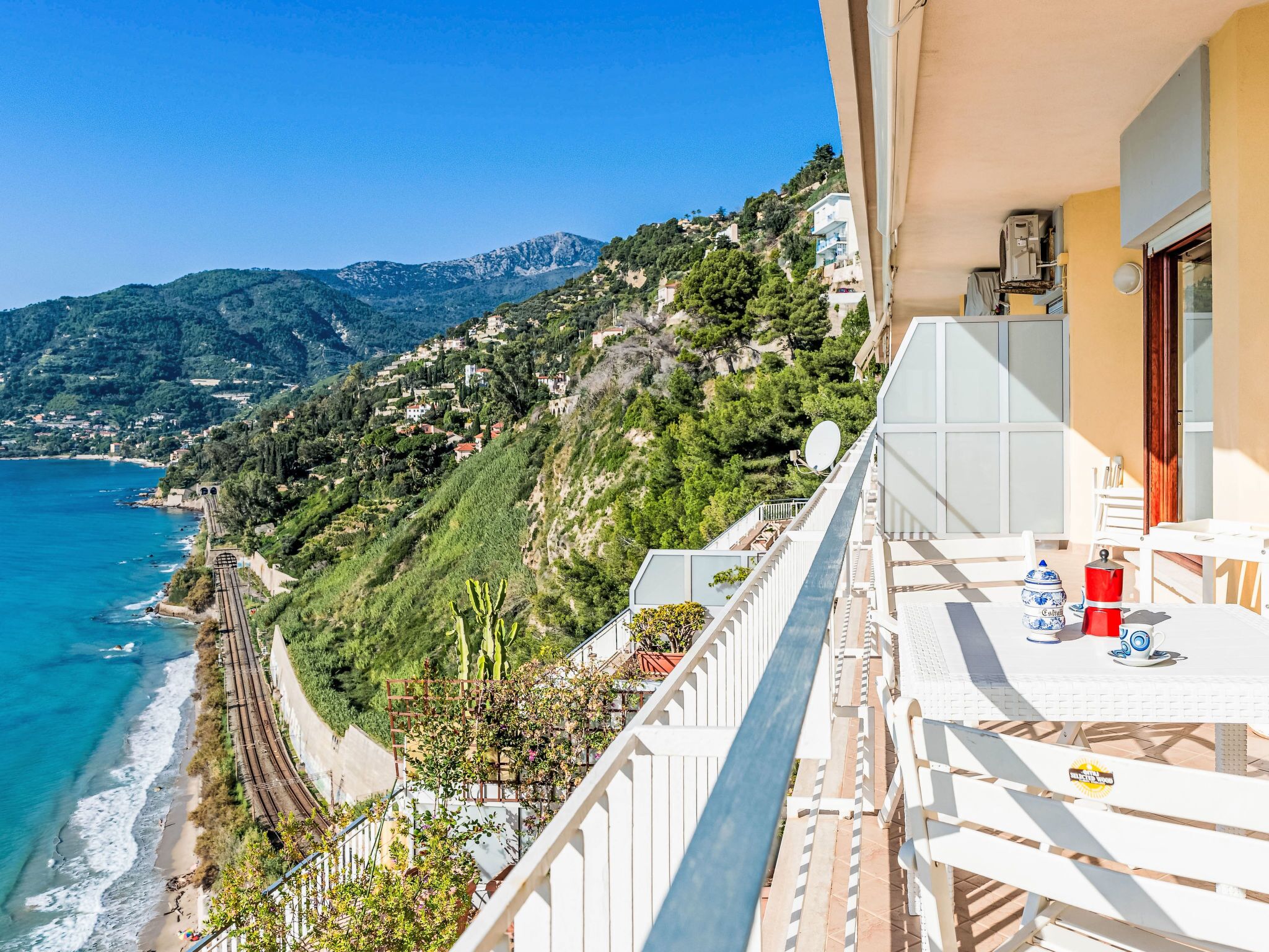 A balcony with a view of a coastal town, a train track, and a mountain in the background.