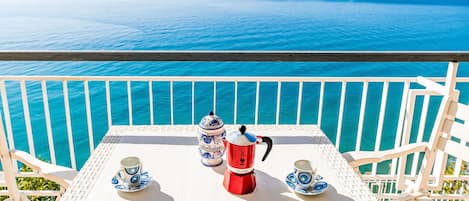 Een tafel met een koffiezetapparaat en kopjes, met uitzicht op een wateroppervlak.