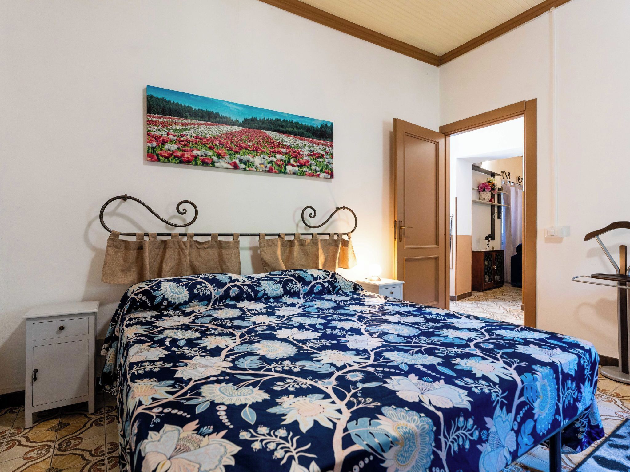 A bedroom with a bed, a nightstand, a dresser, a painting on the wall, and a door leading to another room.