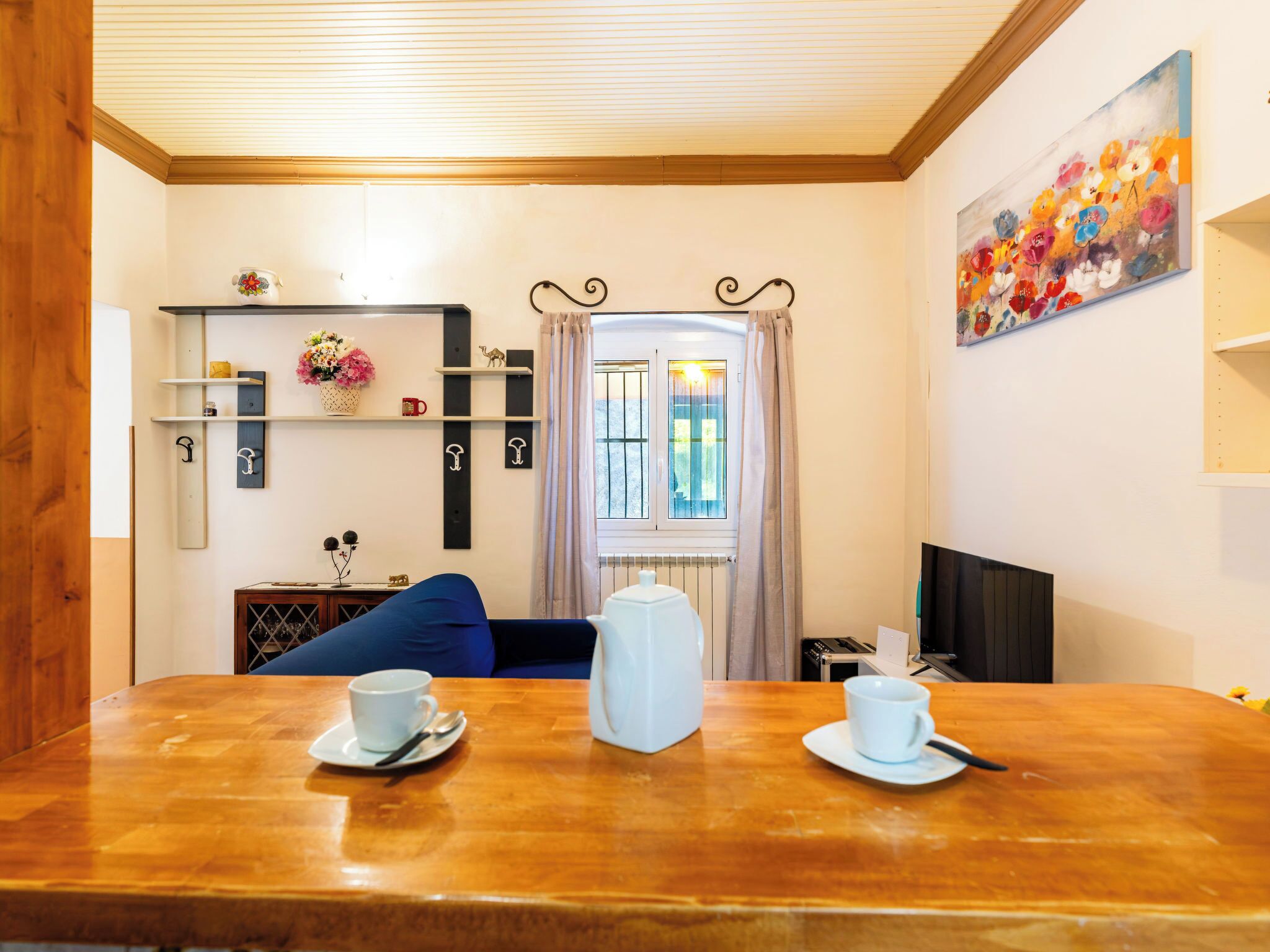 A dining area with a wooden table, two white cups, a white teapot, and a blue sofa.