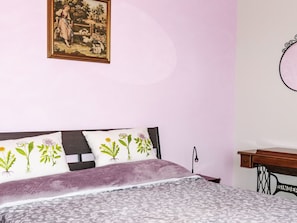 A bedroom with a bed, pillows, a nightstand, a sewing machine, and a wall-mounted mirror. - Casa Mandarino by Interhome (Bordighera)