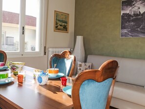 A dining area with a wooden table, chairs, and a view of a building through a window. - Casa Mandarino by Interhome (Bordighera)