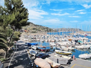 A marina with numerous boats docked, a road with parked cars, and a hilly landscape in the background. - Casa Mandarino by Interhome (Bordighera)