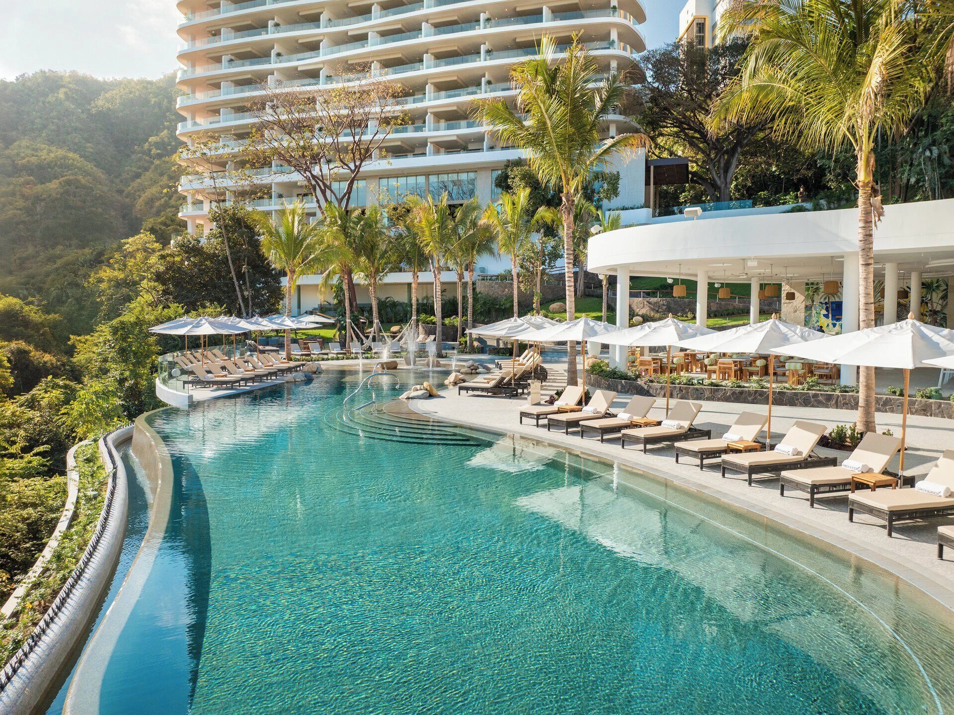 A resort with a large infinity pool, lounge chairs, and a view of a high-rise building.