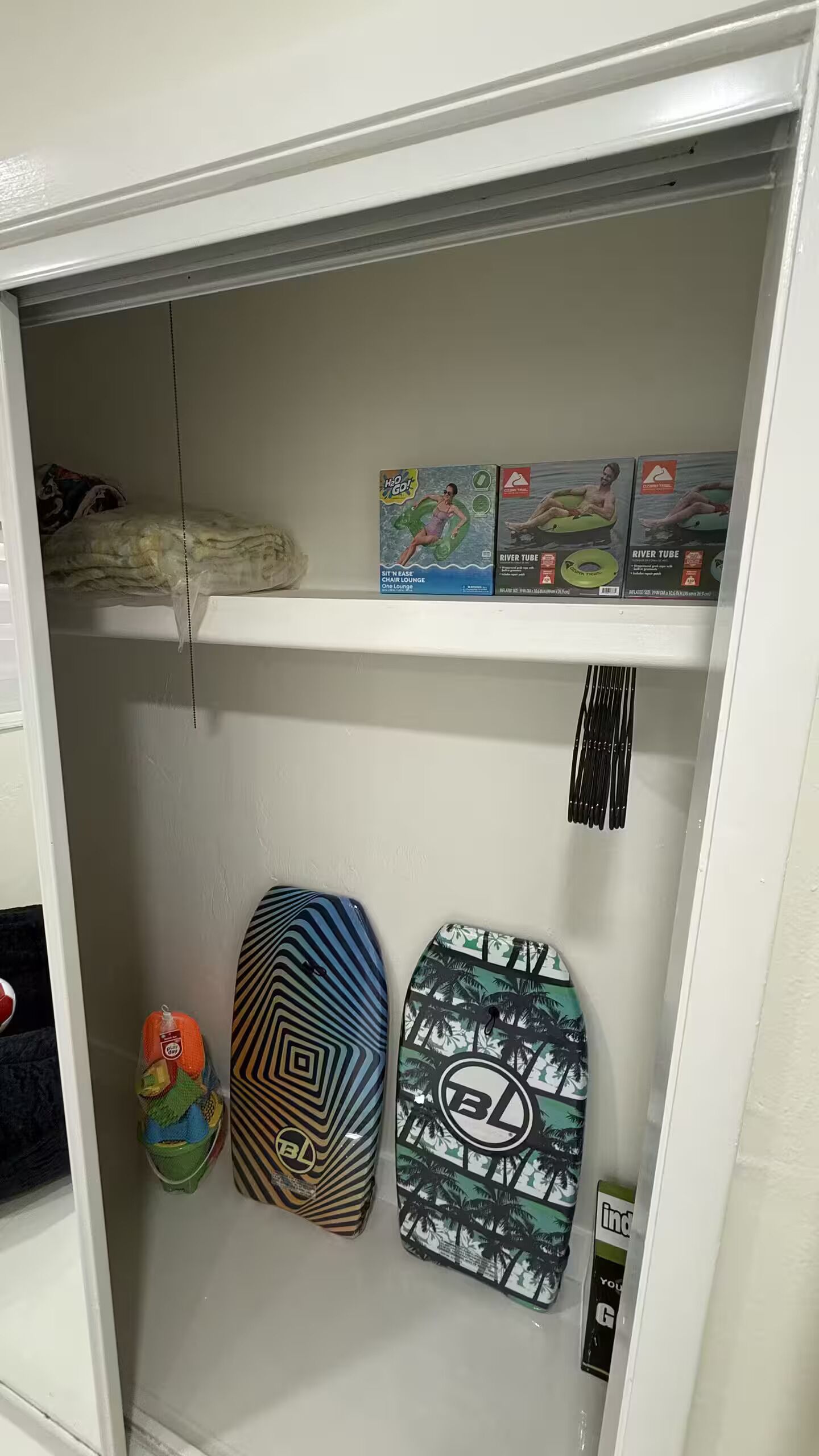 Ein Schrank mit Regalen, der verschiedene Gegenstände wie ein Surfbrett, eine Tasche und eine Kiste beherbergt.