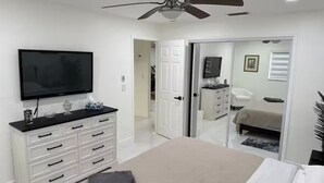 A bedroom with a bed, a television, a ceiling fan, a white dresser, and a closet with a sliding door. - Viceroy 3 bedrooms (Cape Coral)