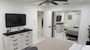 A bedroom with a bed, a television, a ceiling fan, a white dresser, and a closet with a sliding door. - Viceroy 3 bedrooms (Cape Coral)