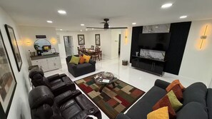 A modern living room with a black leather sofa, a dining area with a wooden table, and a black entertainment unit. - Viceroy 3 bedrooms (Cape Coral)